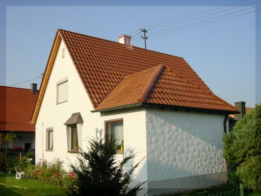 Fertig eingedecktes Dach mit roten Dachziegeln auf einem hellen Wohnhaus