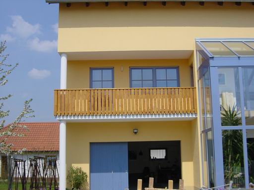 Individuell gefertigter Holzbalkon an einem gelben Wohnhaus